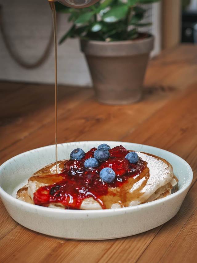 Two fluffy American pancakes topped with fruit compote with fresh fruit drizzled in maple syrup